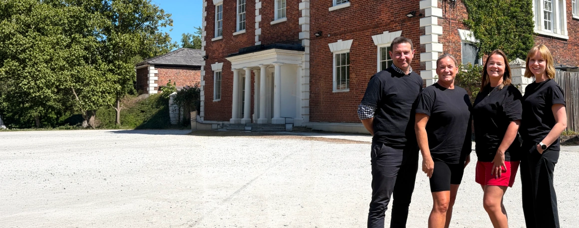 Four key members of the Community Threads team wearing black tops, standing outside Trafford Hall