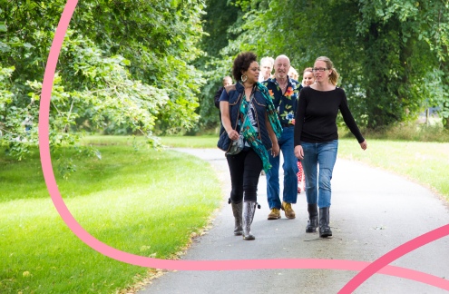 A diverse group of adults walking down a woodland path towards the viewer, through the grounds of Trafford Hall.