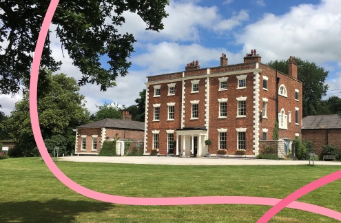 A photograph of Trafford Hall, a former stately home and the new headquarters of Community Threads, sitting within lush, green grounds on a sunny day.